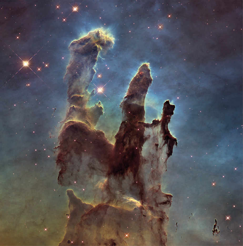 The colored image shows the three grayish black pillars of creation inside the Eagle Nebula. In the background you can see red stars in the black universe. The columns are surrounded by blue nebula.