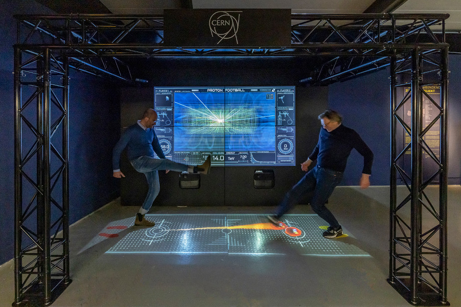Another photo of the same exhibit; two men are kicking the protons projected on the floor at each other like soccer balls.
