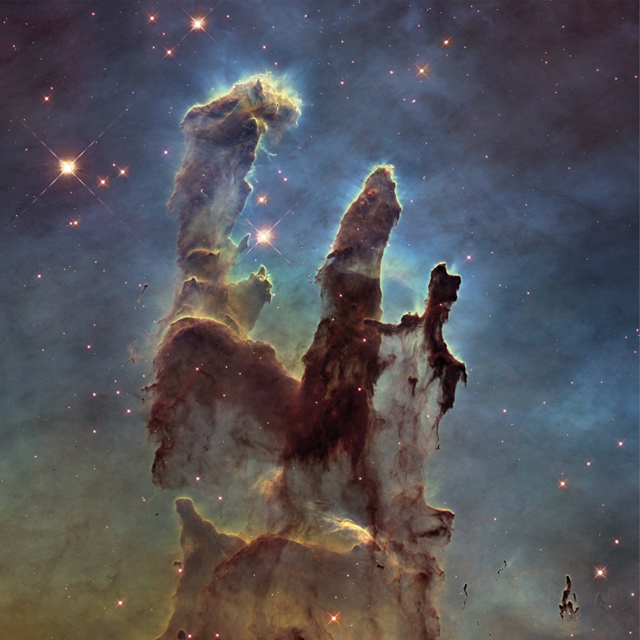 Die farbige Abbildung zeigt die drei grau-schwarzen Säulen der Schöpfung im Adlernebel. Im Hintergrund sieht man rote Sterne im schwarzen Universum. Die Säulen sind von blauem Nebel umgeben.