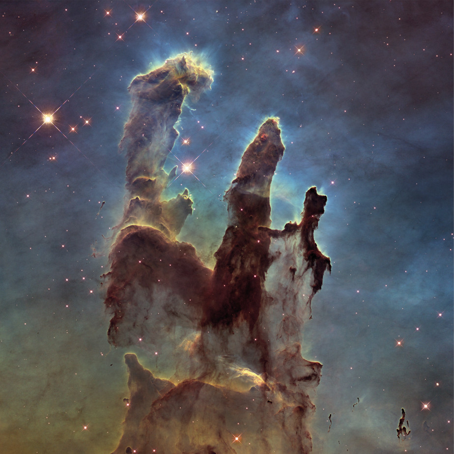 The colored image shows the three grayish black pillars of creation inside the Eagle Nebula. In the background you can see red stars in the black universe. The columns are surrounded by blue nebula.